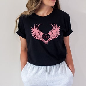May include: Black t-shirt featuring a pink heart with wings design. The heart contains the number 1111.