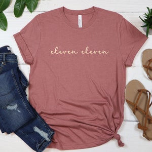May include: A mauve coloured t-shirt with the text "eleven eleven" printed in a light peach colour.