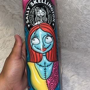 May include: A white stainless steel tumbler with a colourful design featuring Sally from The Nightmare Before Christmas. The design includes a pink background with the text "Sally Skellington" in a black circle. Sally is depicted with her signature red hair, blue skin, and patchwork clothing.
