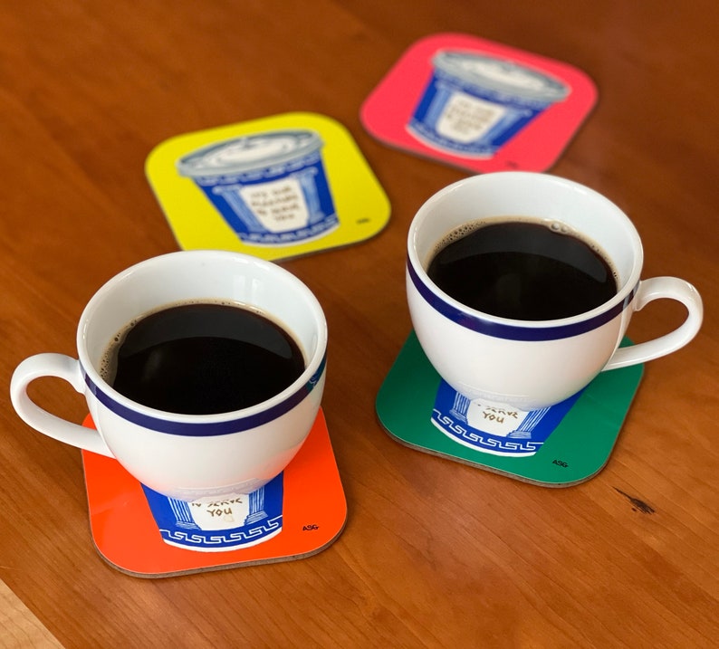 May include: Two white coffee mugs with blue trim, filled with black coffee, sitting on colorful coasters with the text "I love you" in a blue font. The coasters are orange, green, and red.