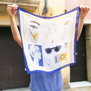 Puede incluir: Un pañuelo de seda blanco con borde azul presenta un diseño dibujado a mano de un perfil de hombre, gafas de sol, un vaso de limonada, una flor en un jarrón y un sol con cara. El pañuelo se sostiene frente al rostro de una persona.