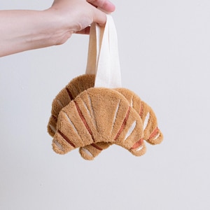 May include: Two plush brown croissant shaped toys with a white fabric loop for hanging.