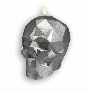 May include: A silver skull-shaped candle with a geometric design. The candle is lit and has a flame.