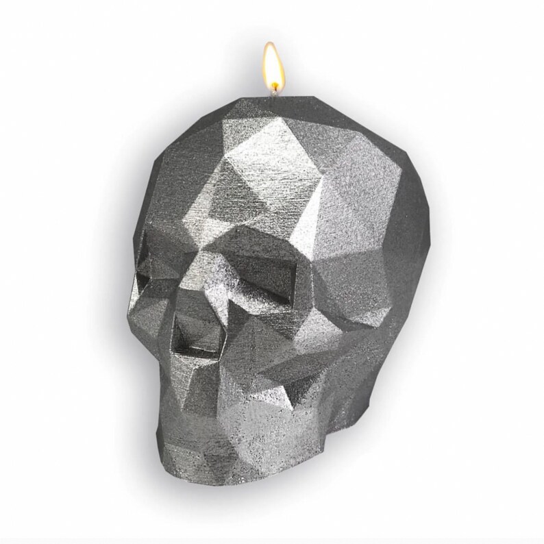 May include: A silver skull-shaped candle with a geometric design. The candle is lit and has a flame.