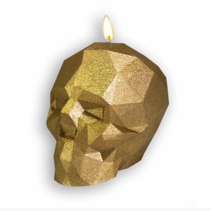 May include: A gold glitter skull-shaped candle with a lit wick.