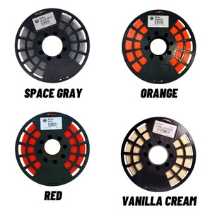 K&ouml;nnte beinhalten: Vier Spulen Filament f&uuml;r den 3D-Druck. Die Spulen sind mit "Space Gray", "Orange", "Rot" und "Vanillecreme" beschriftet.