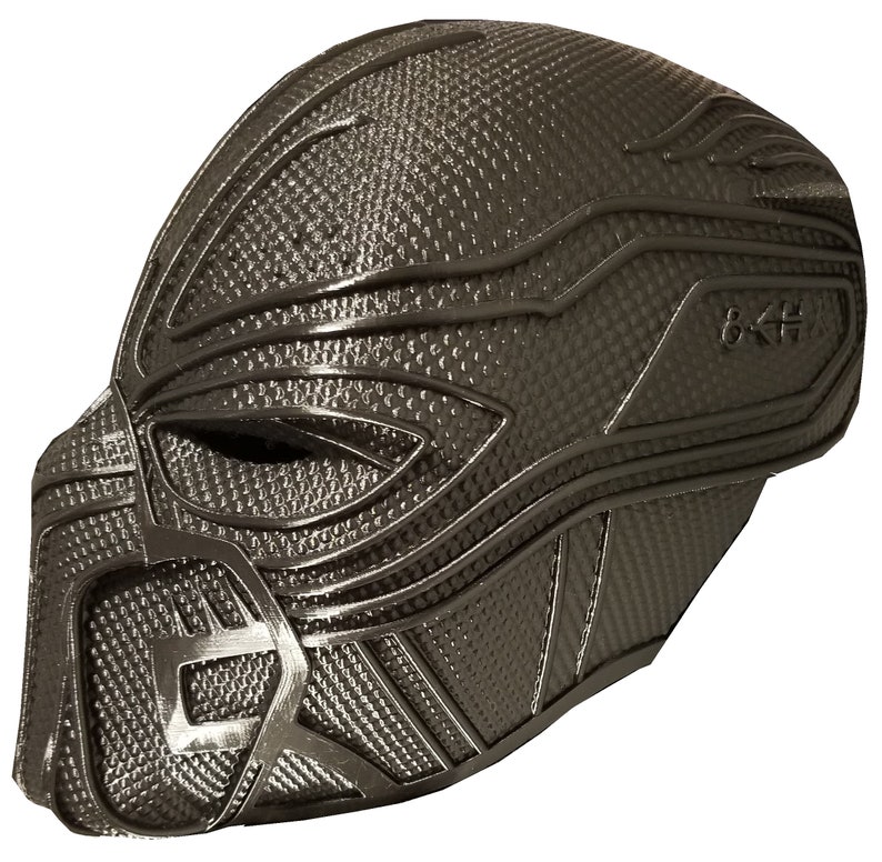 May include: A black plastic 3D printed mask with a textured surface and a geometric design. The mask has a raised ridge around the eyes and a small opening for the mouth.