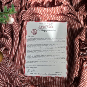 May include: A letter from Santa Claus to Jace, welcoming him to the North Pole and introducing him to his very own Elf. The letter is written on white paper with red and black text and a red and white checked background. The letter is signed "Santa Claus" and includes his address: 325 S. Santa Claus Lane, North Pole, Alaska 90705.