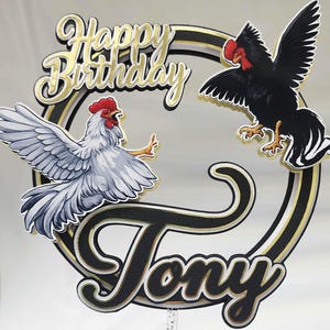May include: A cake topper with a black and gold ring design, featuring two rooster illustrations and the words "Happy Birthday Tony" in gold and black lettering. The rooster illustrations are in black and white.