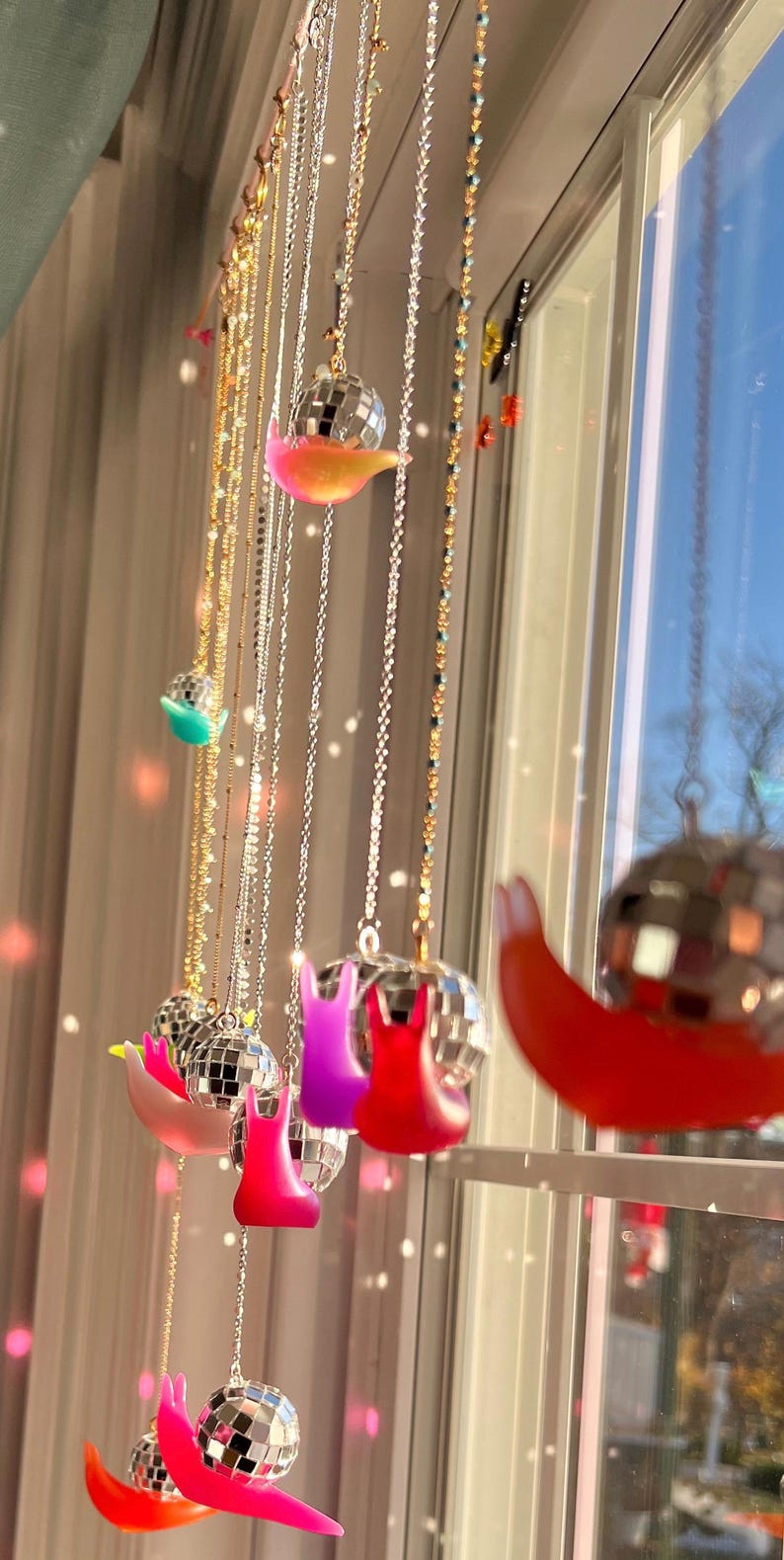 May include: A collection of hanging decorative ornaments. Each ornament features a disco ball and a colorful snail-shaped base. The snails are in various colors, including pink, red, and purple. The ornaments hang from delicate chains.