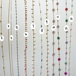 May include: A collection of delicate necklaces with various designs. Some feature small beads in silver and gold, while others showcase colorful gemstones and floral accents. The necklaces are displayed against a white background, highlighting their intricate details.
