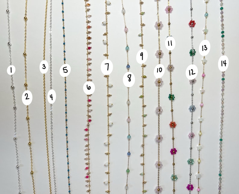 May include: A collection of delicate necklaces with various designs. Some feature small beads in silver and gold, while others showcase colorful gemstones and floral accents. The necklaces are displayed against a white background, highlighting their intricate details.