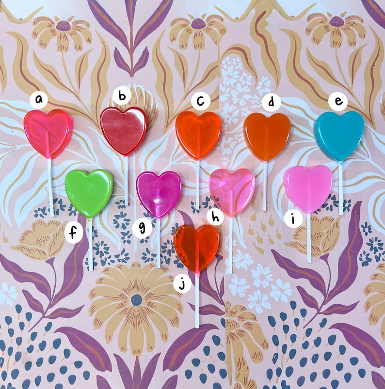 May include: Ten heart-shaped lollipops in shades of pink, red, orange, green, and teal, each on a white stick. The lollipops are displayed against a floral patterned background. A colourful selection of sweets.