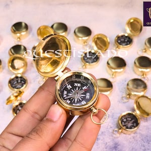 Puede incluir: Una brújula de latón con una cara negra y una tapa de color dorado. La brújula está rodeada de muchas otras brújulas de latón, todas cerradas.