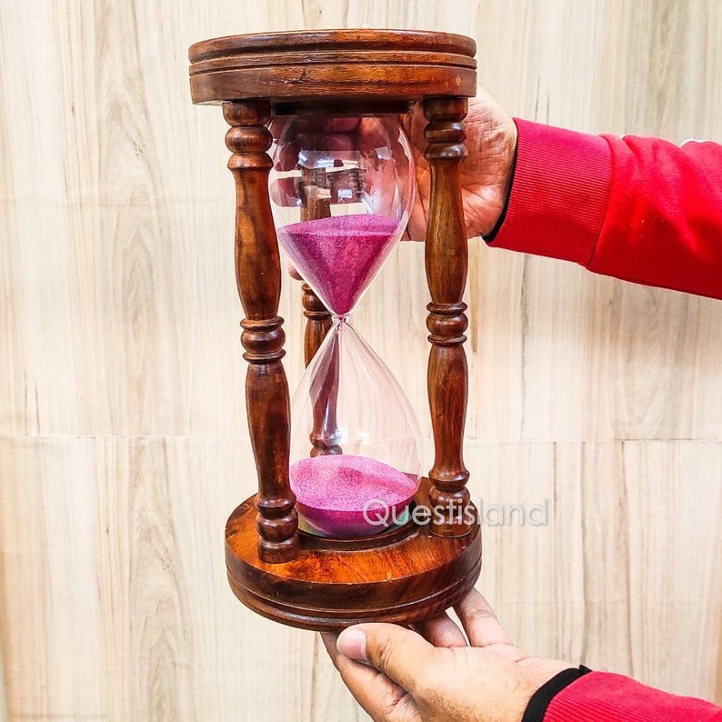 May include: A wooden hourglass with a pink sand timer. The hourglass is made of dark wood and has a classic design.