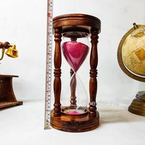 May include: A wooden hourglass with a clear glass bulb and pink sand. The hourglass is approximately 10 inches tall and has a wooden base.