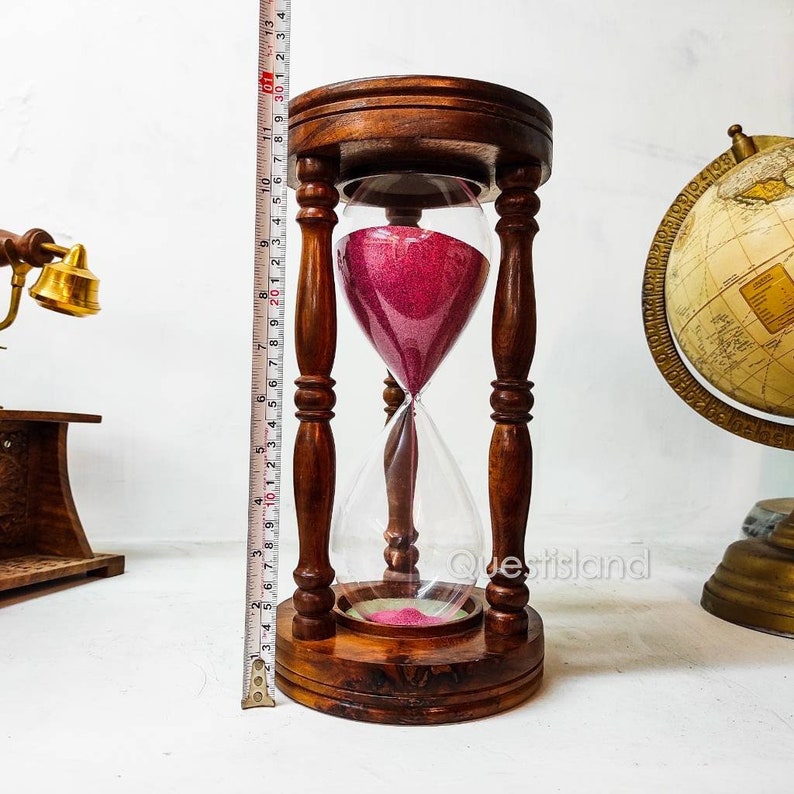 May include: A wooden hourglass with a clear glass bulb and pink sand. The hourglass is approximately 10 inches tall and has a wooden base.