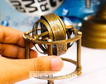 Op de afbeelding: Een messing model van een hemelbol met een draaibare arm en een voet. De bol is gegraveerd met dierenriemtekens en sterrenbeelden. Het model is een decoratief stuk voor thuis of op kantoor.