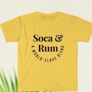 May include: A yellow t-shirt with the words "Soca & Rum" in a black, stylized font. The text is arranged in a circular design, with "A WORLD-CLASS BLEND" curving around the bottom. The shirt is a casual wear item.