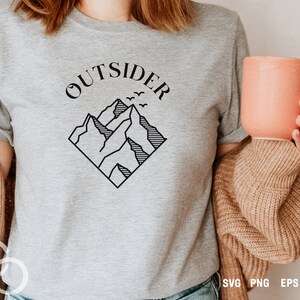 May include: A gray t-shirt with the text "OUTSIDER" in black lettering above a black line drawing of mountains with birds flying over them.