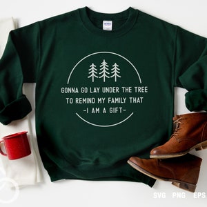 May include: A dark green sweatshirt with a white circle design featuring three stylized trees and the text "GONNA GO LAY UNDER THE TREE TO REMIND MY FAMILY THAT -I AM A GIFT-"