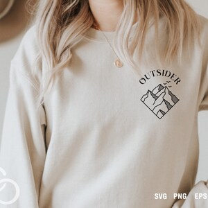 May include: A white sweatshirt with a black graphic design of mountains and the word "OUTSIDER" in a circle above the mountains.