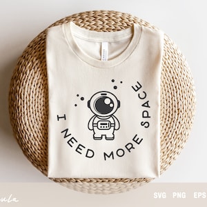 Könnte beinhalten: Ein weißes T-Shirt mit einer Schwarzweißillustration eines Astronauten mit dem Text "I need more space" in einem Kreis um den Astronauten.