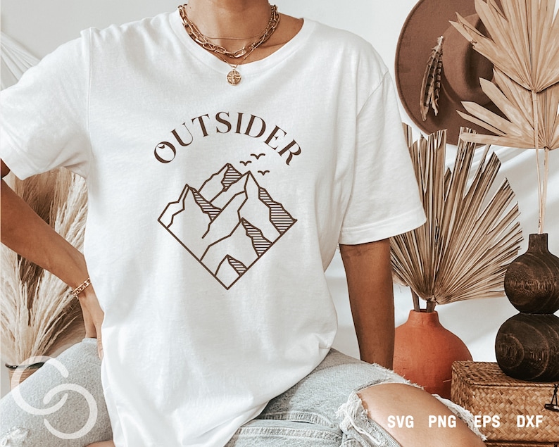 May include: White t-shirt with a brown graphic of mountains and the word "OUTSIDER" above the mountains.