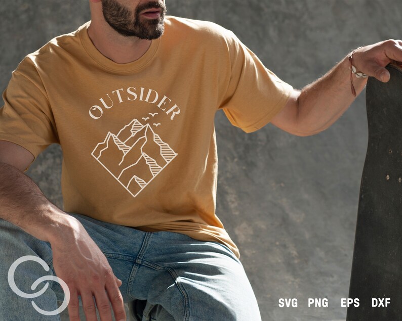 May include: A person wearing a mustard yellow t-shirt with a white graphic of mountains and the word "OUTSIDER" above the mountains. The person is holding a skateboard.