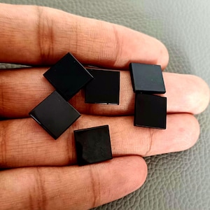 Könnte beinhalten: Sechs schwarze quadratische Edelsteine, wahrscheinlich Onyx, werden auf einer Hand gezeigt. Die Edelsteine sind glatt und poliert.