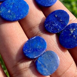 Op de afbeelding: Een verzameling ovale en ronde lapis lazuli cabochons in verschillende maten. De stenen zijn diepblauw met witte aderen en vlekken van gouden pyriet.