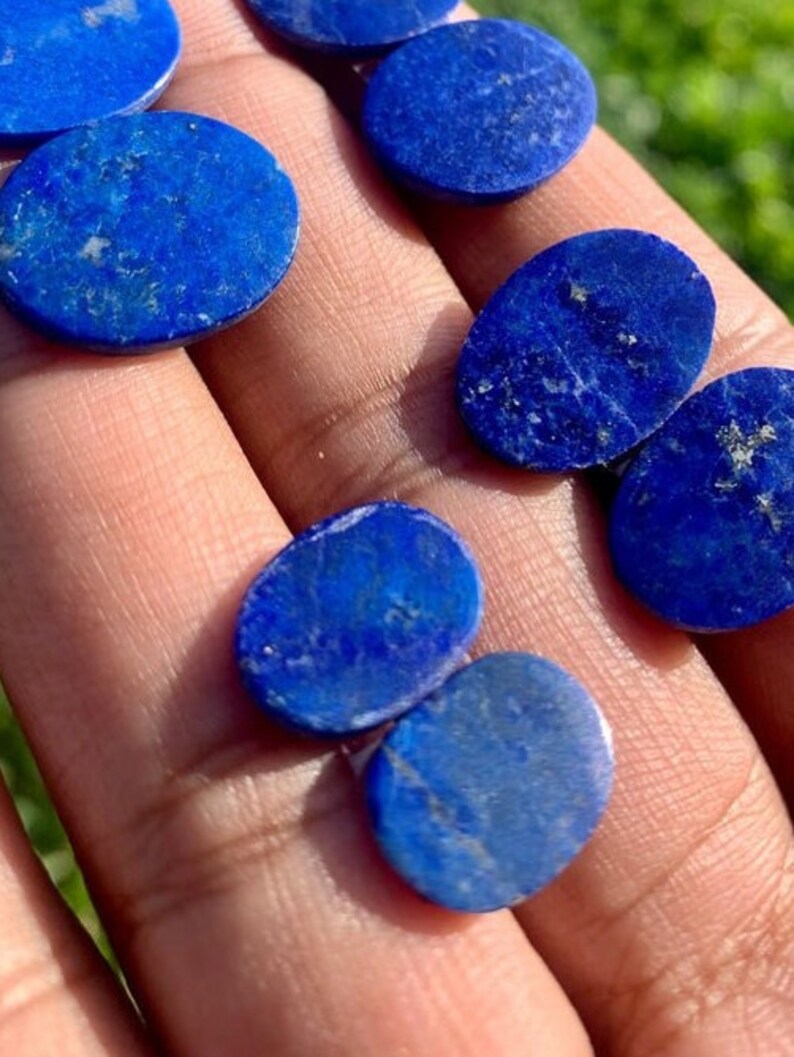 Op de afbeelding: Een verzameling ovale en ronde lapis lazuli cabochons in verschillende maten. De stenen zijn diepblauw met witte aderen en vlekken van gouden pyriet.