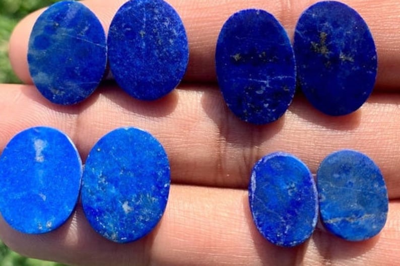 Op de afbeelding: Acht ovale lapis lazuli cabochons in verschillende tinten blauw met vlekken van gouden pyriet.