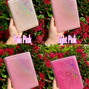 May include: Four Kindle Paperwhite cases in different shades of pink: pale pink, light pink, lilac pink, and magenta pink. Each case has a clear, glittery design.
