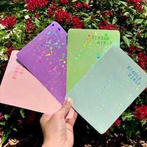 May include: Four different colored notebooks with a holographic finish and the text "Kindle Girly" printed on each.