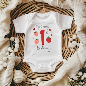 Może przedstawiać: Białe body niemowlęce z napisem "My Berry 1st Birthday" w czarnym skrypcie. Cyfra "1" jest czerwona, wraz z grafikami truskawek i serc. Body z krótkim rękawem ma zapięcie na zatrzaski.