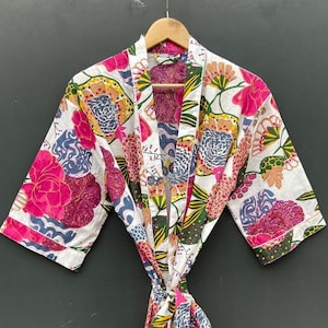 Puede incluir: Una bata de algodón blanca con estampado floral de colores. La bata tiene un cinturón de atar y mangas largas.