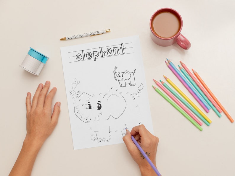 K&ouml;nnte beinhalten: Ein Kind verbindet die Punkte, um einen Elefanten auf einem wei&szlig;en Blatt Papier zu zeichnen. Das Papier hat oben das Wort "Elefant" geschrieben. Das Kind verwendet einen lila Stift, um die Punkte zu verbinden. Auf dem Tisch liegen auch verschiedene farbige Stifte und eine Tasse Kaffee.