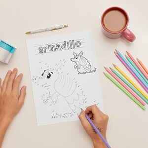K&ouml;nnte beinhalten: Ein Kind verbindet die Punkte auf einer Punkt-zu-Punkt-Malvorlage mit einem G&uuml;rteltier. Die Seite ist mit "armadillo" betitelt. Das Kind verwendet einen lila Stift, um die Punkte zu verbinden. Auf dem Tisch liegen auch farbige Stifte.