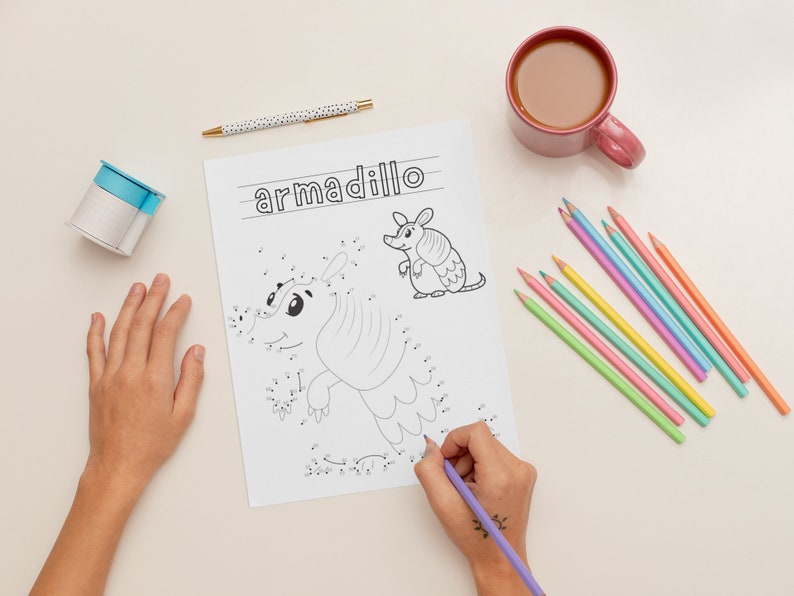 K&ouml;nnte beinhalten: Ein Kind verbindet die Punkte auf einer Punkt-zu-Punkt-Malvorlage mit einem G&uuml;rteltier. Die Seite ist mit "armadillo" betitelt. Das Kind verwendet einen lila Stift, um die Punkte zu verbinden. Auf dem Tisch liegen auch farbige Stifte.