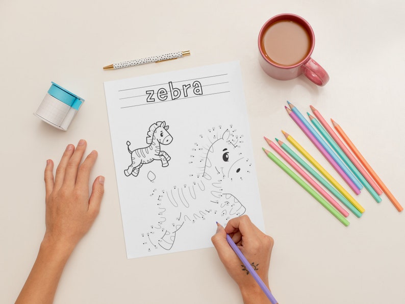 K&ouml;nnte beinhalten: Ein Kind verbindet die Punkte auf einer Schwarzwei&szlig;zeichnung eines Zebras auf einem wei&szlig;en Blatt Papier. Das Wort "Zebra" steht oben auf der Seite. Das Kind verwendet einen violetten Stift, um die Punkte zu verbinden. Auf dem Tisch liegen verschiedene farbige Stifte.