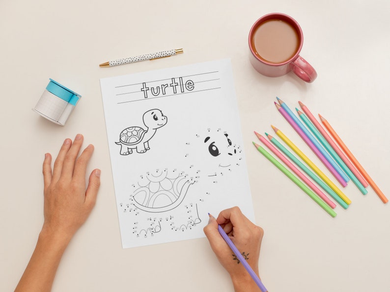 K&ouml;nnte beinhalten: Eine Kinderhand zeichnet ein Punkt-zu-Punkt-Bild einer Schildkr&ouml;te. Das Bild befindet sich auf einem wei&szlig;en Blatt Papier mit dem Wort "turtle" oben. Auf dem Tisch liegen auch farbige Stifte und eine Tasse Kaffee.