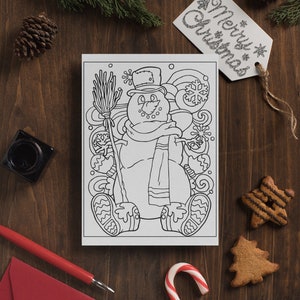 May include: A black and white coloring page featuring a snowman with a hat, scarf, and broom. The snowman is surrounded by snowflakes and swirls. The page is on a wooden table with a red envelope, a candy cane, and gingerbread cookies.