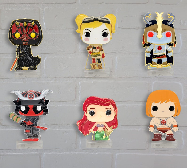 Op de afbeelding: Zes verschillende popcultuur-figuurtjes, elk met een uniek ontwerp en kleurenschema. De figuurtjes worden getoond op een witte bakstenen muur. De personages zijn Darth Maul, Harley Quinn, een personage uit Masters of the Universe, Deadpool, Ariel uit The Little Mermaid en He-Man.
