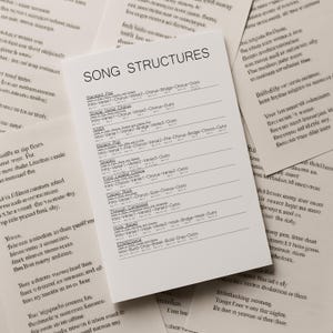 Könnte beinhalten: Ein weißes Blatt Papier mit der Überschrift "SONG STRUCTURES" listet verschiedene Songformate auf, wie z. B. "Standard Pop" und "Classic Rock". Das Papier ist von anderen Papierblättern mit handschriftlichem Text umgeben.