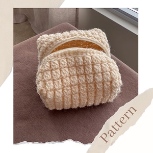 May include: A cream-coloured, crocheted pouch with a textured, bubble-like pattern. The pouch is open, revealing a glimpse of the interior. The word "Pattern" is visible in the lower right corner. This handmade item is likely a cosmetic bag or small storage accessory.