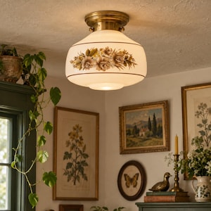 May include: A flush mount ceiling light fixture featuring a brass base and a white glass dome shade. The shade is decorated with a horizontal band of brown and tan floral illustrations, including roses and leaves, accented by thin brown lines.
