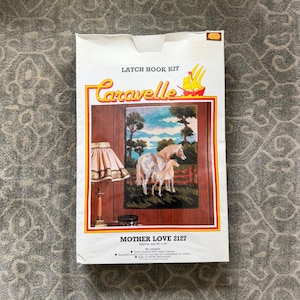 May include: A white Caravelle latch hook kit featuring a finished rug design of two horses. The kit includes the text "Mother Love 2127" and the approximate size of the finished rug is 20" x 30". The kit is packaged in a white box with yellow and red accents.