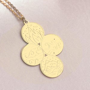 Puede incluir: Collar de oro con un colgante que presenta cuatro dijes circulares, cada uno con un diseño diferente. Los dijes están conectados en forma de racimo. El collar está sobre un fondo blanco.