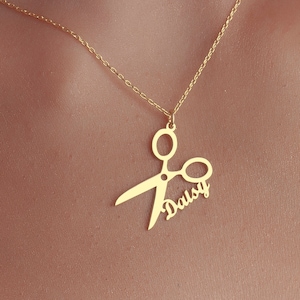 May include: Gold necklace with a scissor pendant and the name "Daisy" written inside the scissor blades.